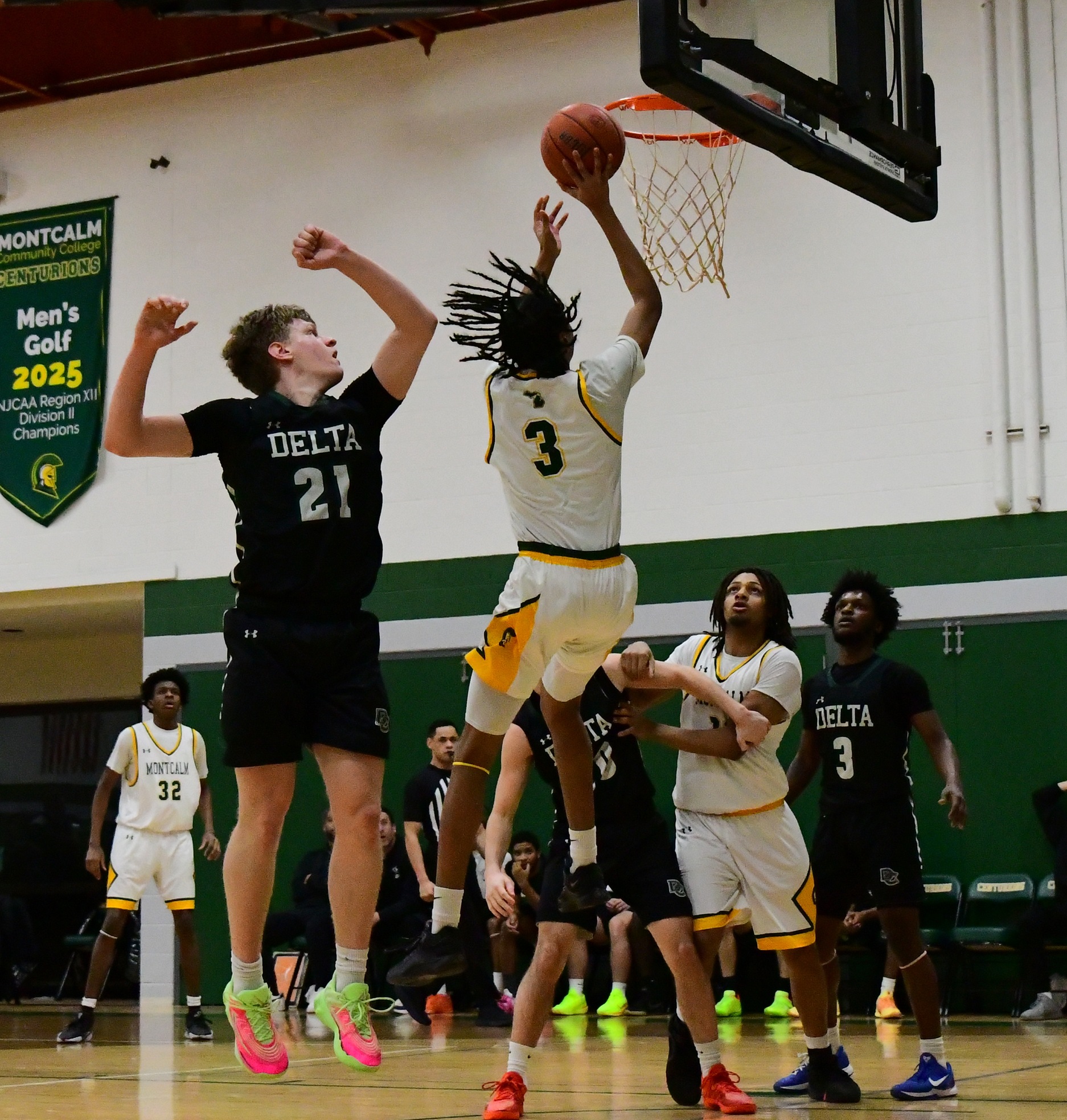 MCC men's basketball player shooting a layup while an opposing player jumps behind him.