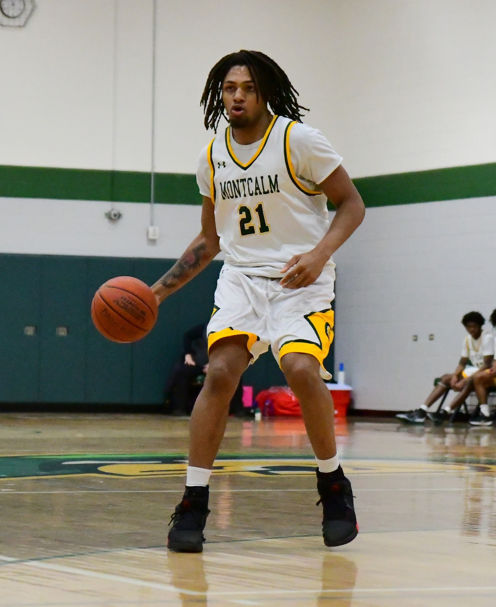 MCC men's basketball player dribbling the ball on the court during a game. His jersey number is 21.