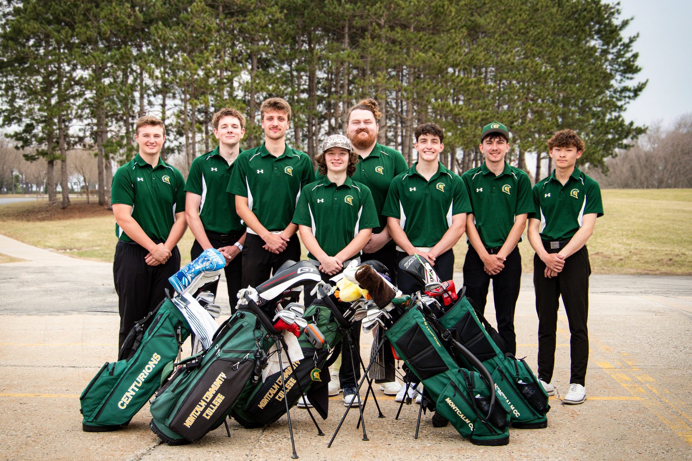 Men's golf team outside with golf bags in front of them.