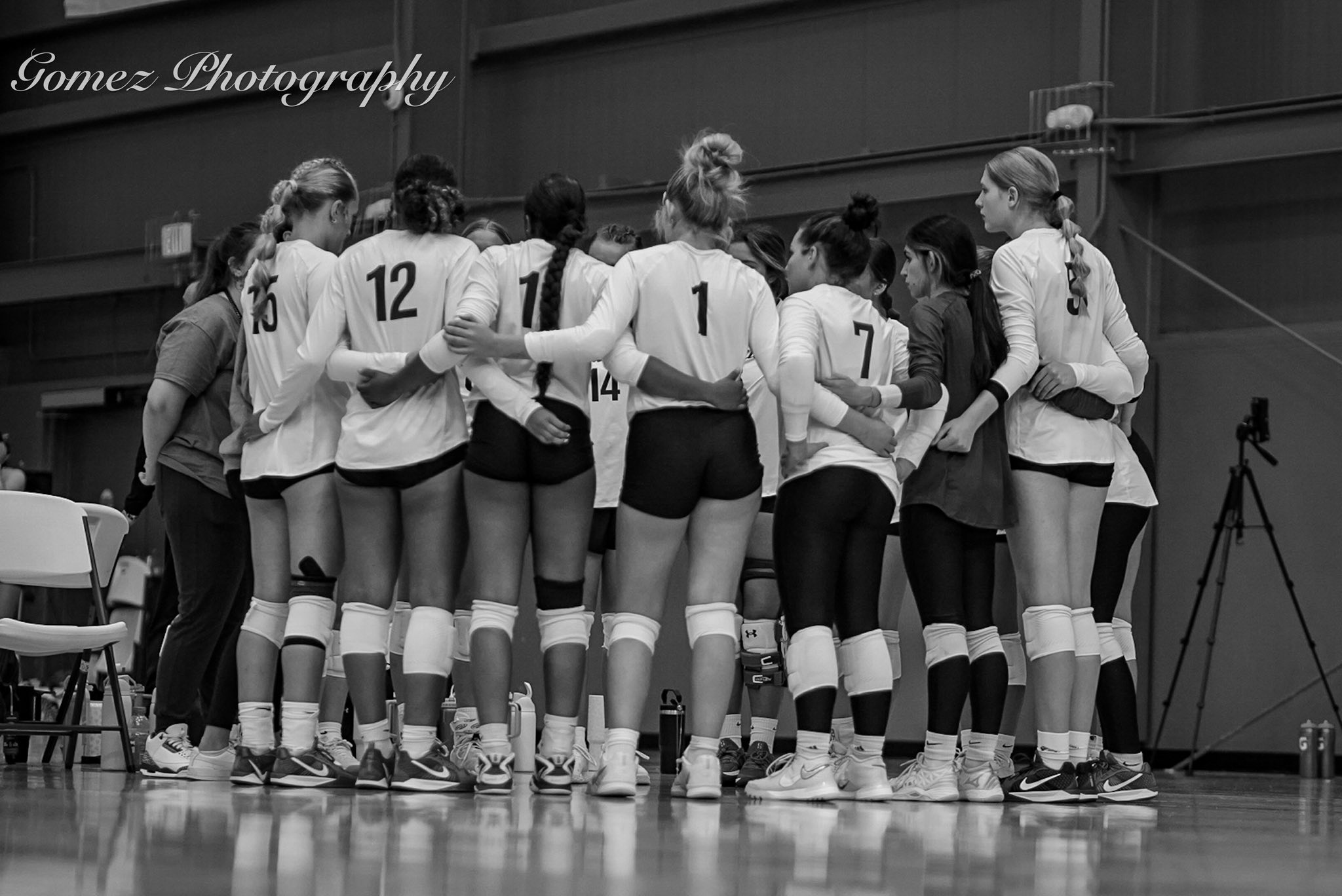 Black and white photo of the women's volleyball team standing on the court with arms around eachother.